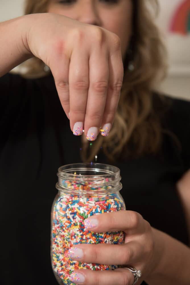woman sprinkling sprinkles into a jar of sprinkles