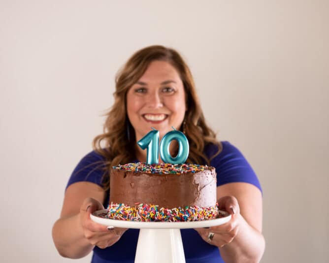 woman holding chocolate birthday cake with teal number 10 candles on white cake plate