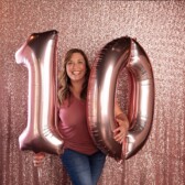 woman in pink shirt holding pink number balloons 10 with pink backdrop
