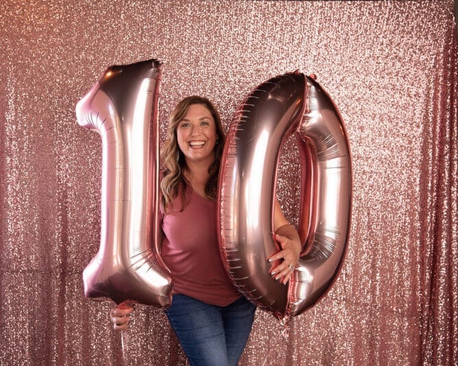 woman in pink shirt holding pink number balloons 10 with pink backdrop