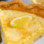 Slice of lemon chess pie on a scalloped plate with silver fork with recipe title on top of image