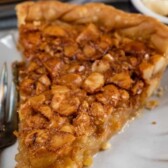 One slice of macadamia nut pie on a white scalloped plate with recipe title on top of image