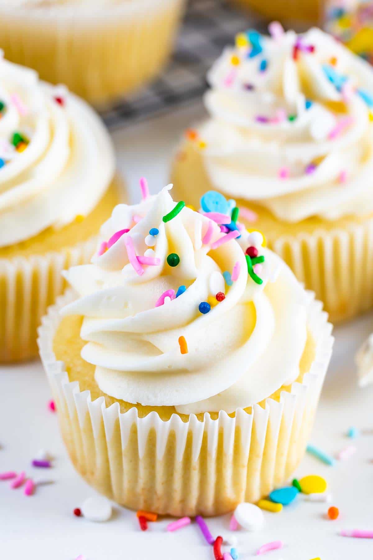 Yellow cake cupcakes with vanilla frosting and sprinkles on top and around bottom