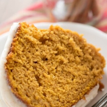 One slice of pumpkin bundt cake on a white plate with silver fork with recipe title on top of image