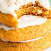 Stack of pumpkin cookies with cream cheese frosting with a bite missing out of one cookie and recipe title on top of photo