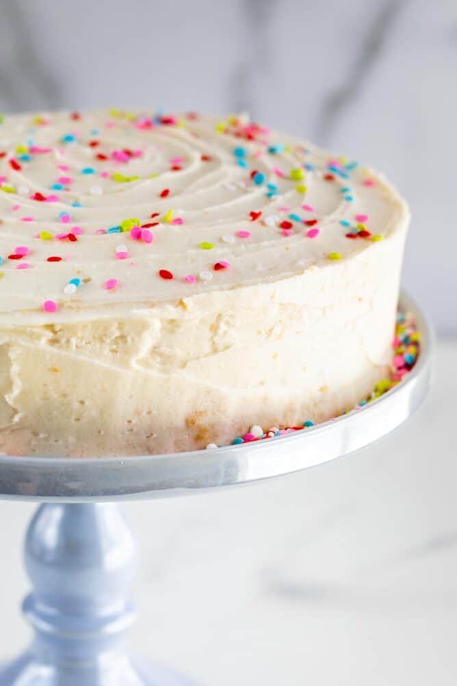 Yellow layered cake on a cake stand with vanilla buttercream and rainbow sprinkles