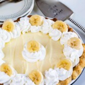 Overhead shot of banana cream pie ready to serve with place settings and spatula