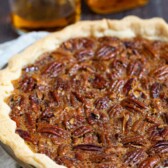 Bourbon pecan pie in pie dish with bourbon bottle and glass behind pie