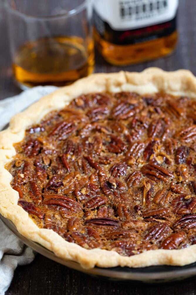 Bourbon pecan pie in pie dish with bourbon bottle and glass behind pie