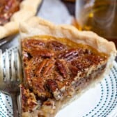 One slice of bourbon pecan pie on a white plate with blue dotted border and silver fork