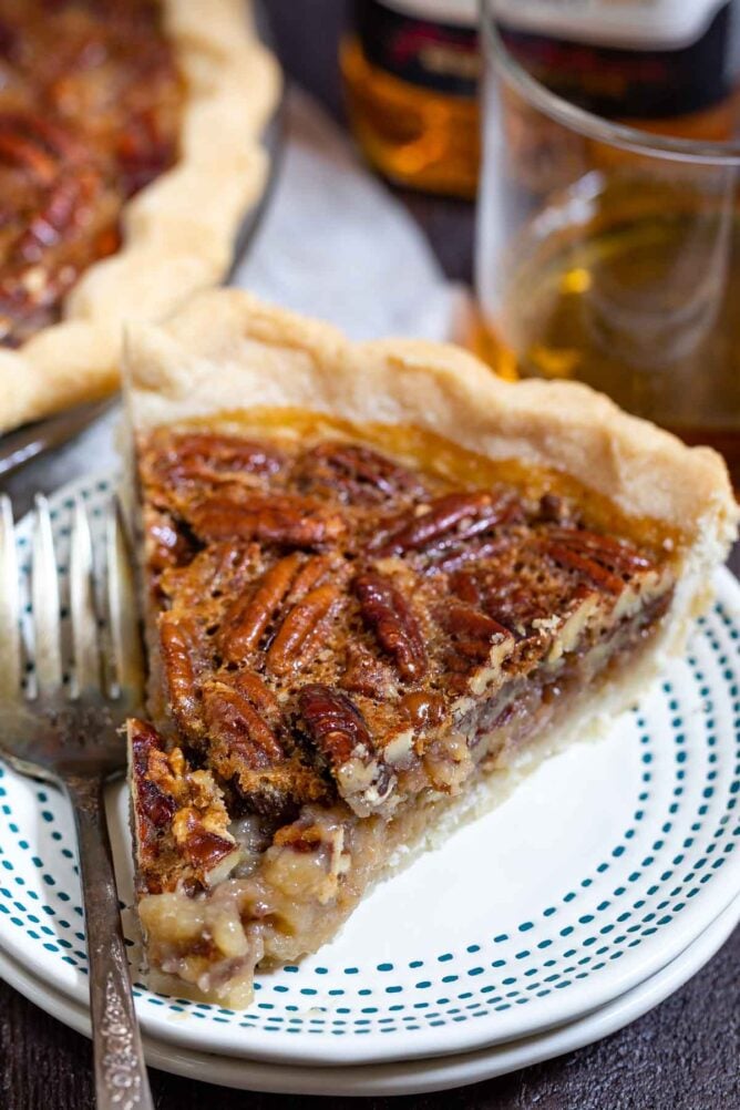 One slice of bourbon pecan pie on a white plate with blue dotted border and silver fork