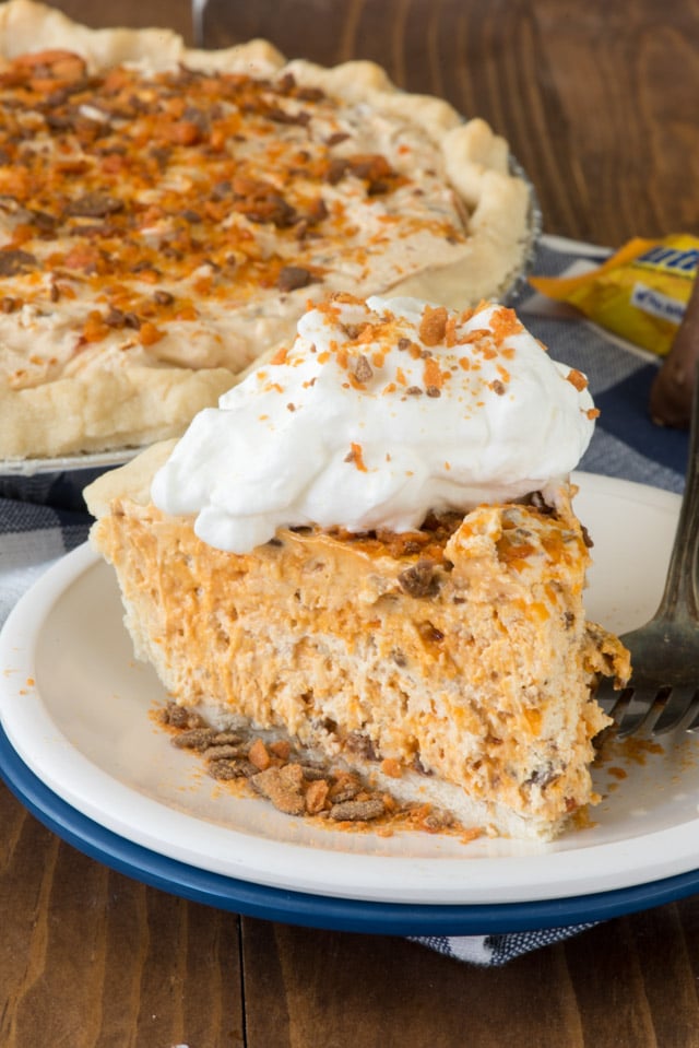 Slice of butterfinger pie on a white and blue plate with rest of pie in background