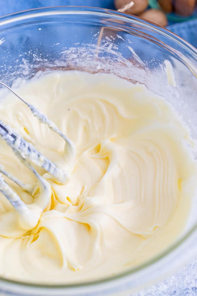 Overhead shot of eggnog frosting being whisked in clear mixing bowl