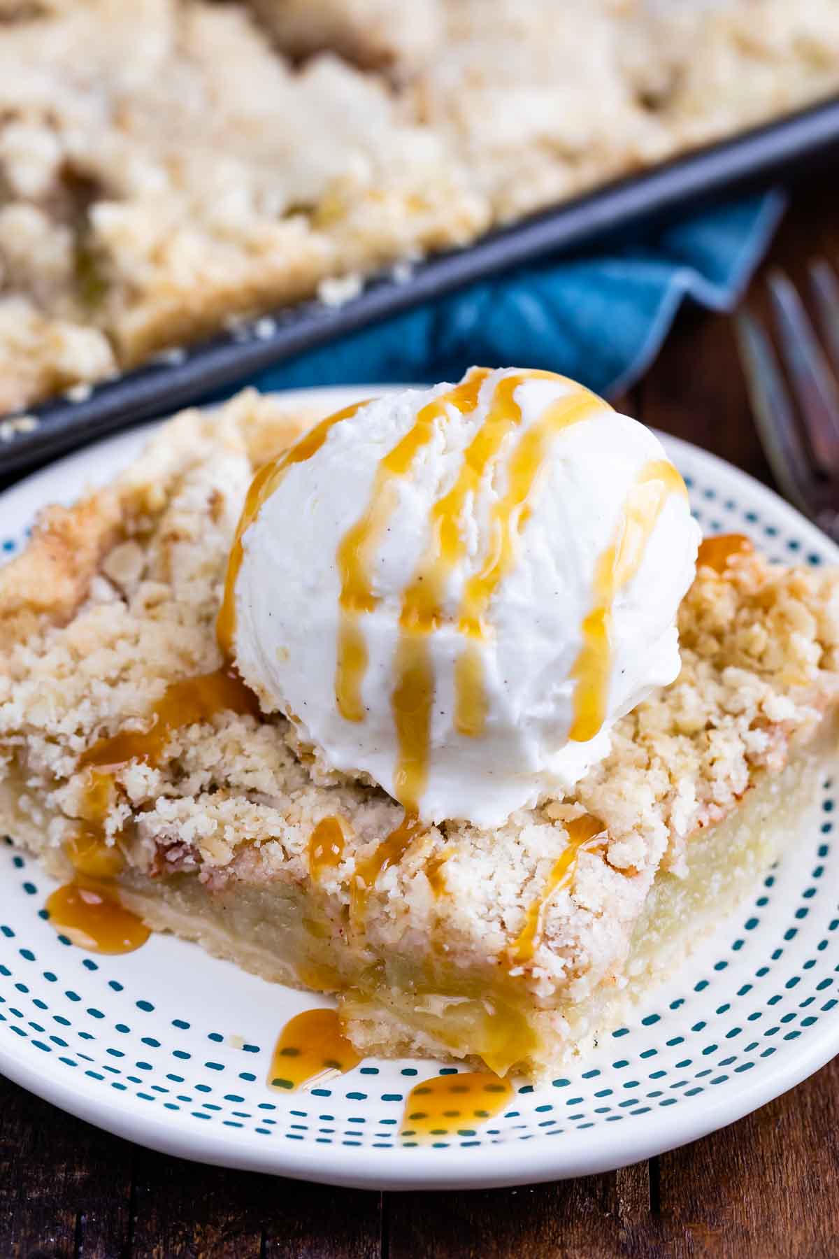 slice of square apple pie on white plate with ice cream and caramel sauce