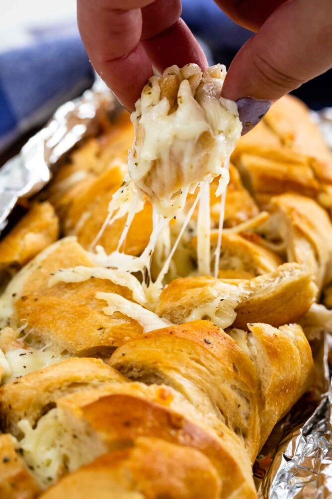 hand pulling piece of French bread with cheese