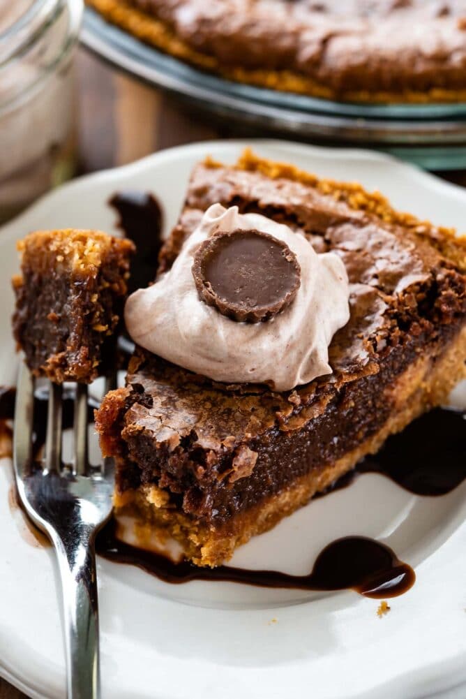 slice of chocolate pie with graham crust on white plate with hot fudge with bite missing