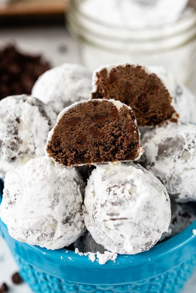 snowball cookies stacked in blue bowl with one cut open to show the inside