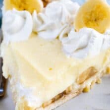 Slice of banana cream pie on grey scalloped plate with recipe title on top of image