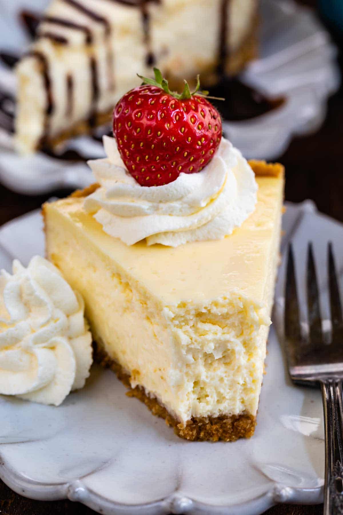 Slice of classic cheesecake with whipped cream and strawberry on top with one bite missing