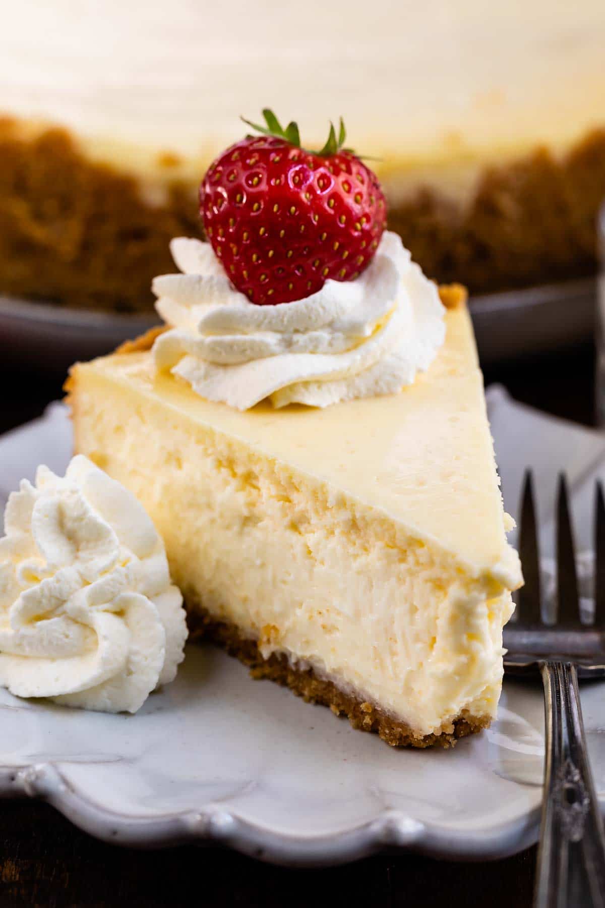 A slice of classic cheesecake on a plate with whipped cream and a strawberry on top