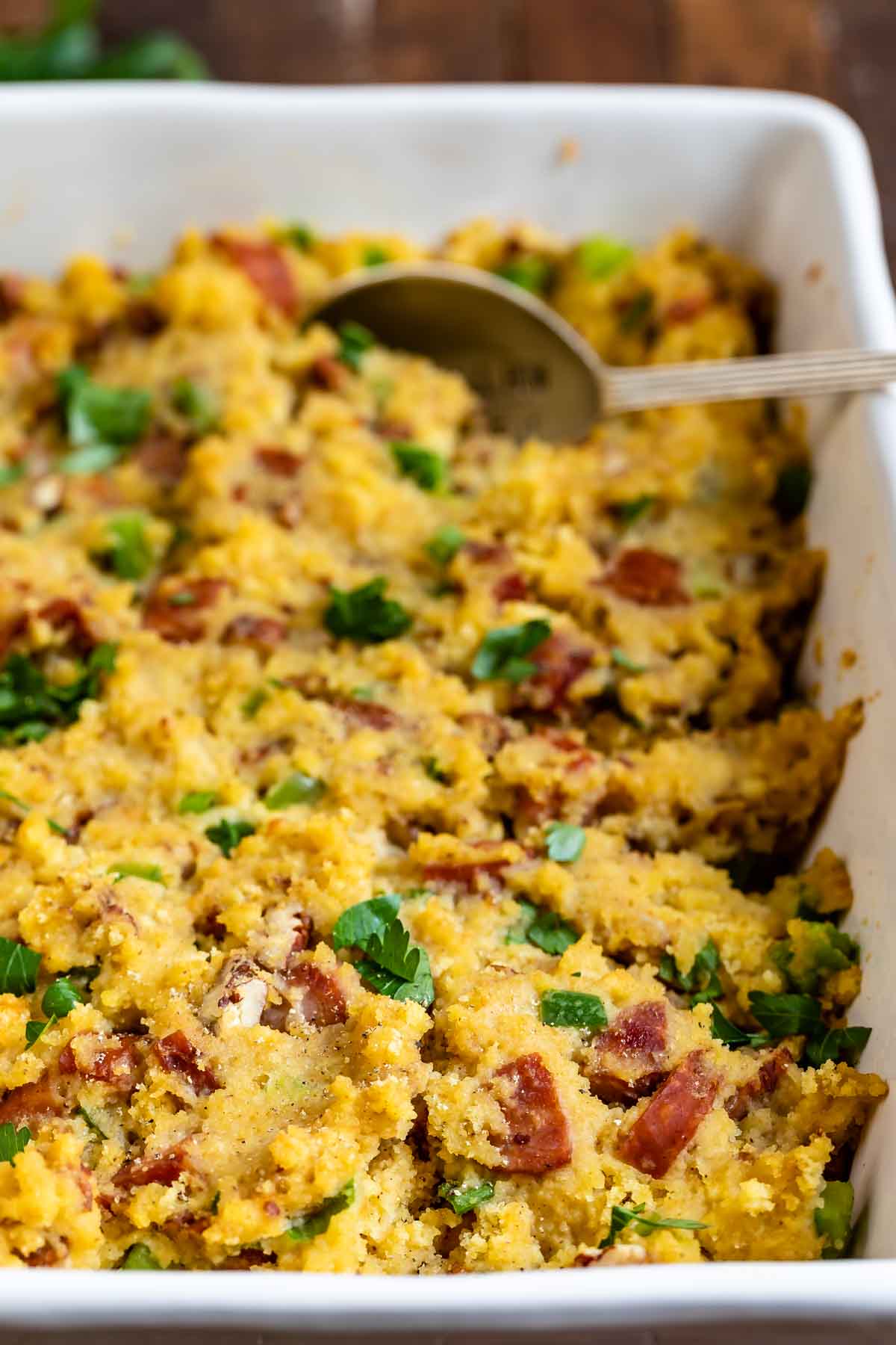 Close up photo of cornbread sausage in white dish with serving spoon