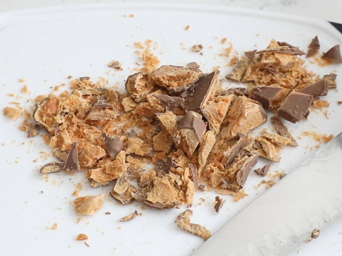 chopped Butterfingers on white cutting board with knife.