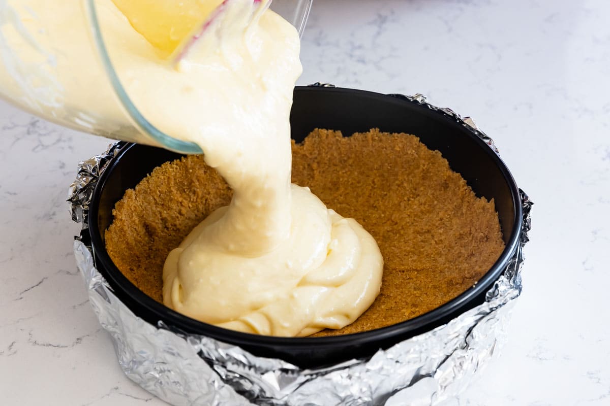 Classic cheesecake filling being poured onto the graham cracker crust