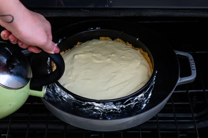 Pouring water around cheesecake pan in oven