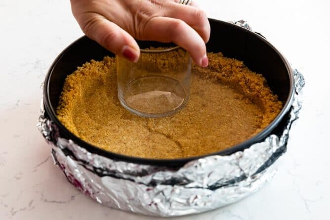 Graham cracker crust being pressed into cheesecake springform pan