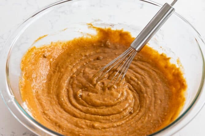 Pumpkin cupcake batter in clear mixing bowl with whisk