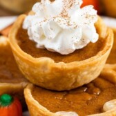 Close up photo of mini pumpkin pies stacked on top of eachother and the top one has whipped cream and recipe title on top of photo