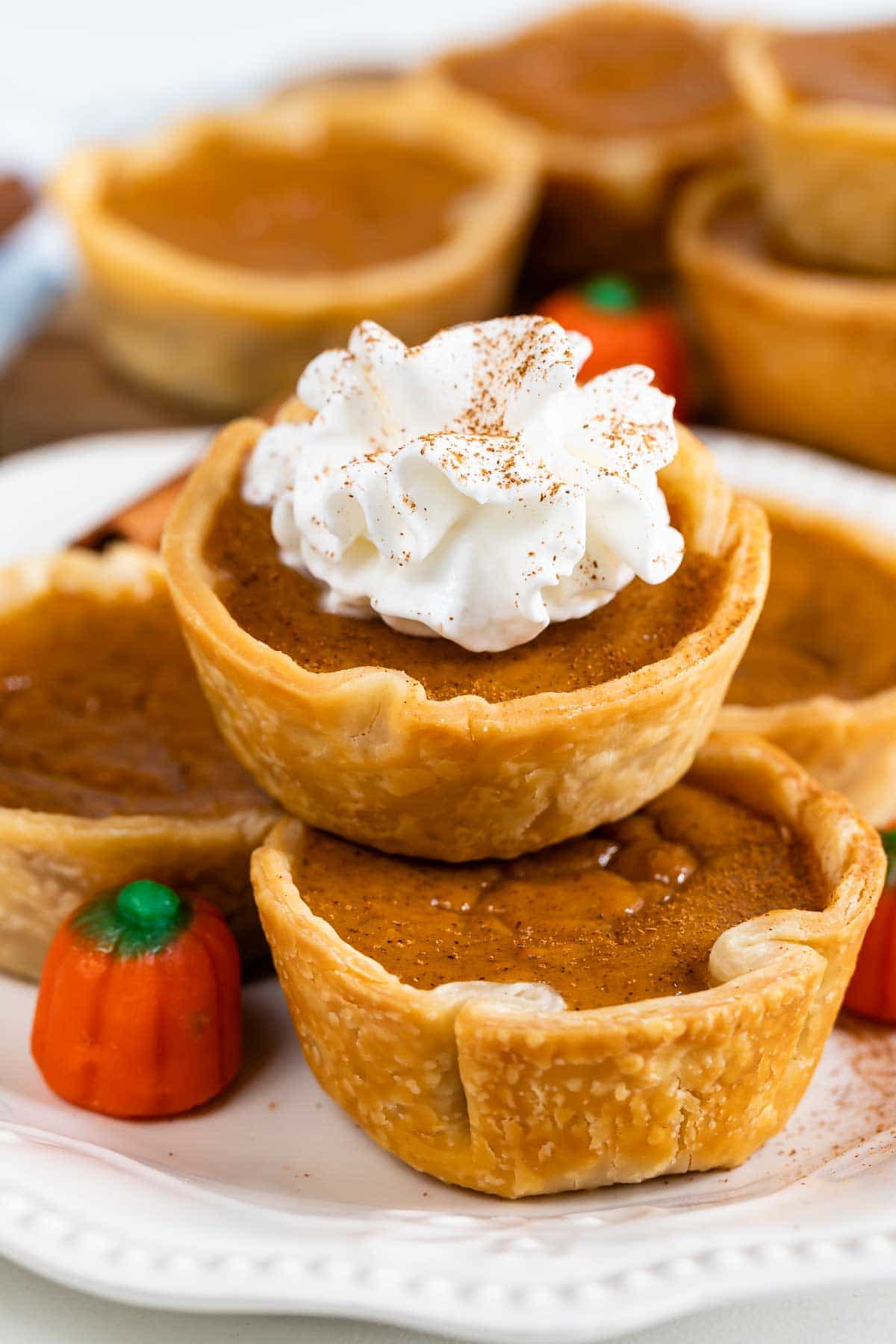 Close up photo of mini pumpkin pies stacked on top of eachother and the top one has whipped cream
