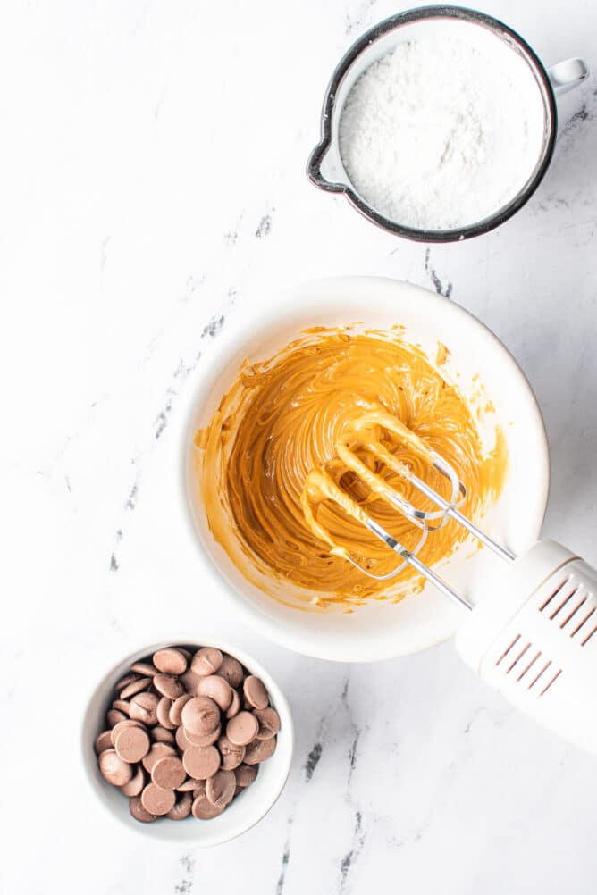 Overhead view of peanut butter mixture being mixed with chocolate and powdered sugar next to it