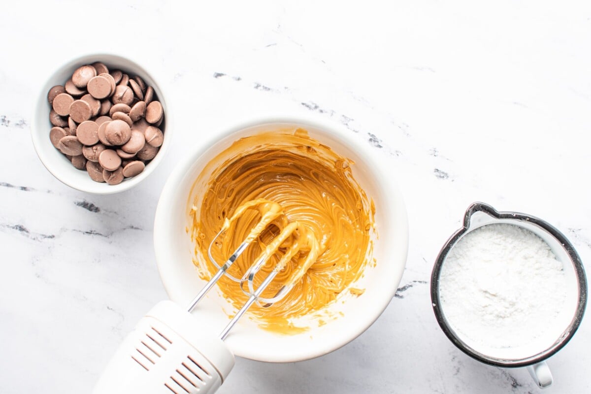 Overhead view of peanut butter mixture being mixed with chocolate and powdered sugar next to it