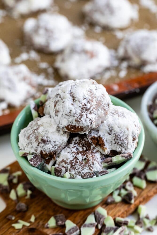 Mint colored bowl full of mint snowball cookies with ingredients around the bowl