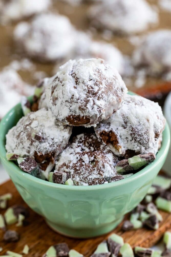 Side view of mint colored bowl full of mint snowball cookies with ingredients around the bowl