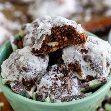 Mint colored bowl full of mint snowball cookies with ingredients around the bowl and one snowball cut in half to show filling