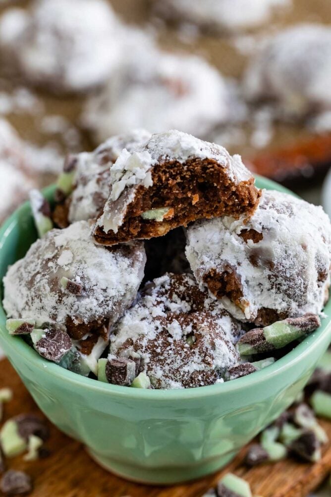 Mint colored bowl full of mint snowball cookies with ingredients around the bowl and one snowball cut in half to show filling