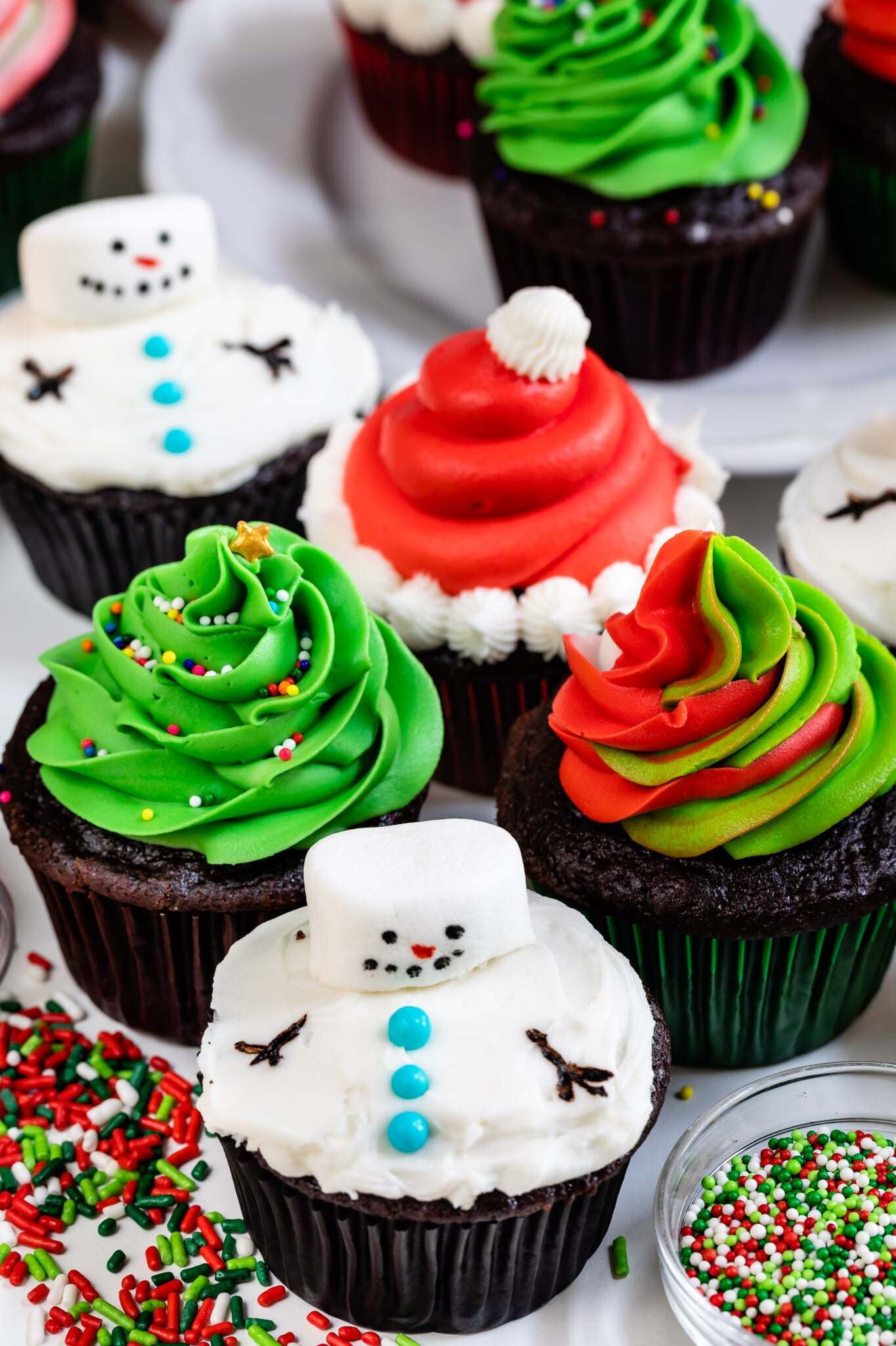 4 cupcakes decorated for christmas: snowman, Santa, swirled frosting, tree