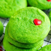 Grinch cookies stacked on a metal wire rack after cooling with recipe title on top of image