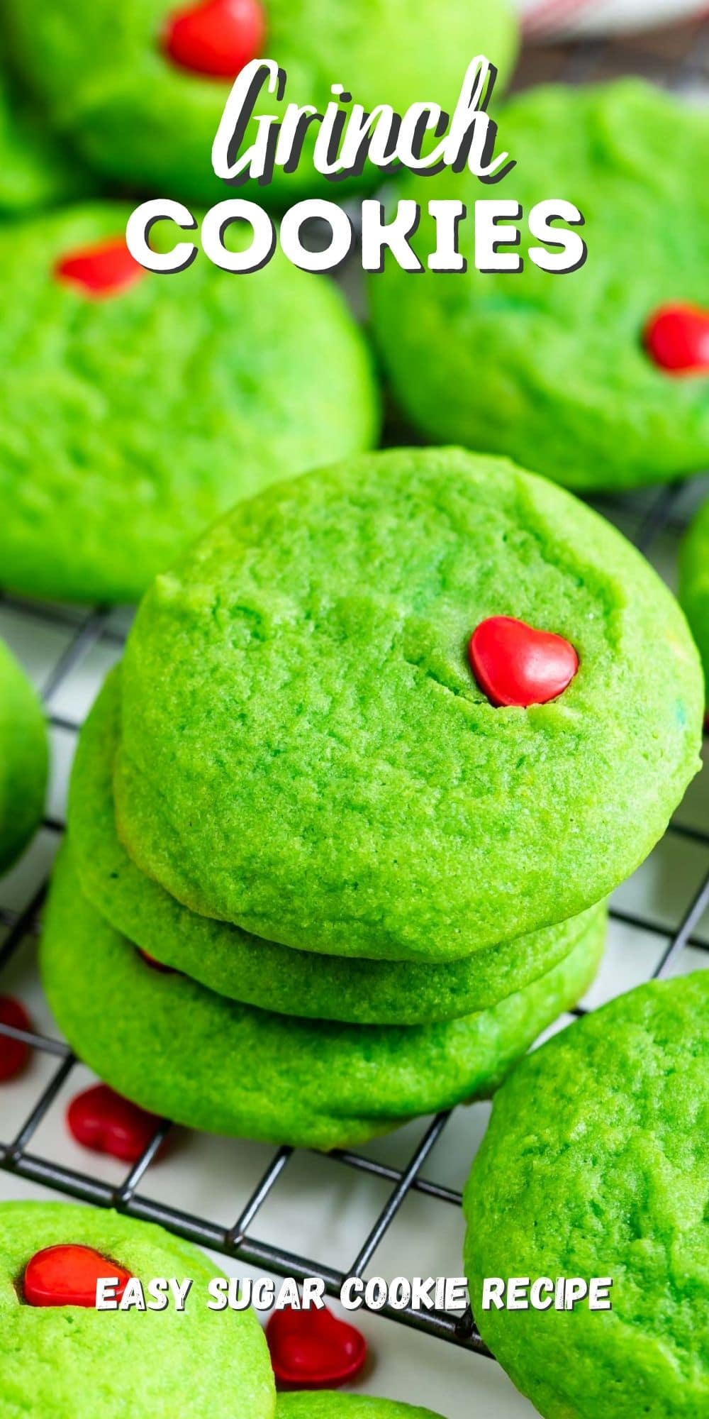 Grinch cookies stacked on a metal wire rack after cooling with recipe title on top of image