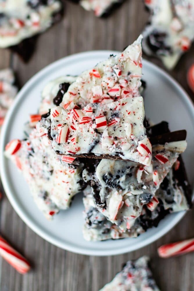 Overhead view of Oreo peppermint bark pieces on a white cake stand with candy canes and more bark below on counter