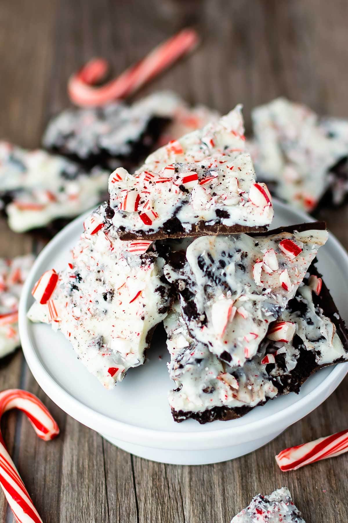 Oreo peppermint bark pieces on a white cake stand with candy canes and more bark below on counter