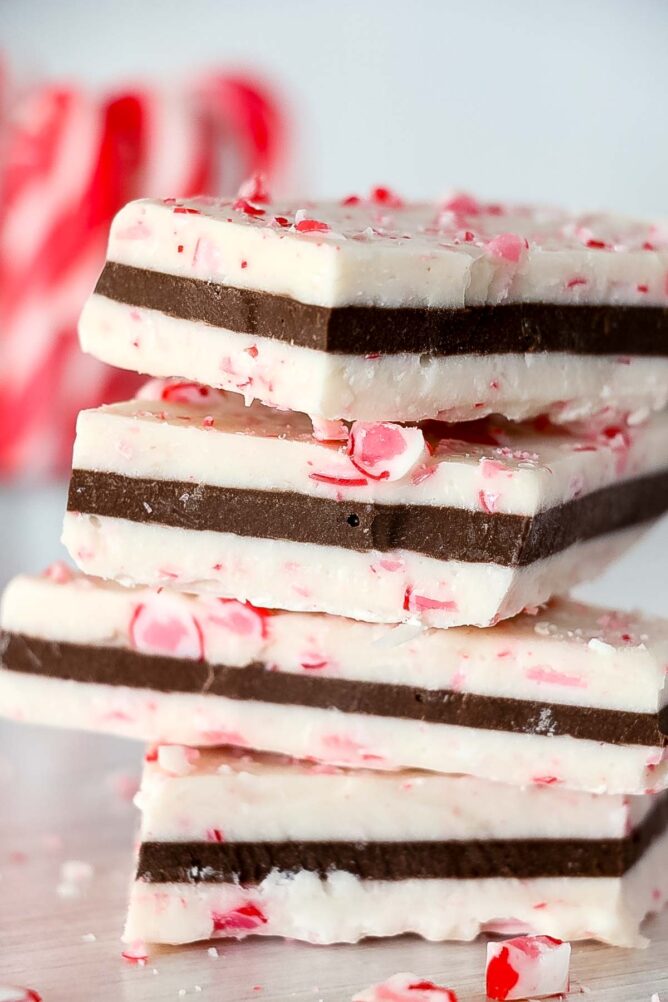 Four peppermint bark pieces stacked on top of eachother with candy canes in background