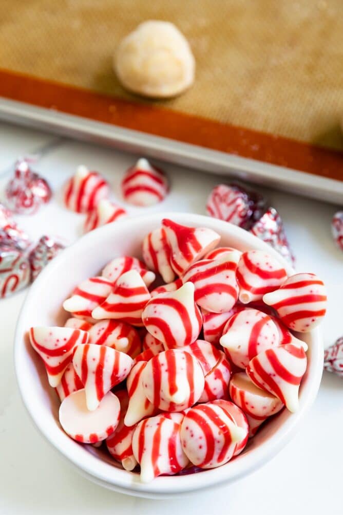 Bowl of peppermint hershey kisses next to sheet pan with peppermint blossom cookie dough balls