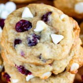 Close up shot of stacked cranberry white chocolate cookies on a wood cutting board with recipe title on top of image