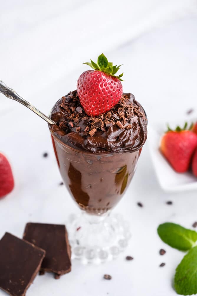 Glass pudding dish of avocado chocolate mousse with chocolate shavings and a strawberry on top