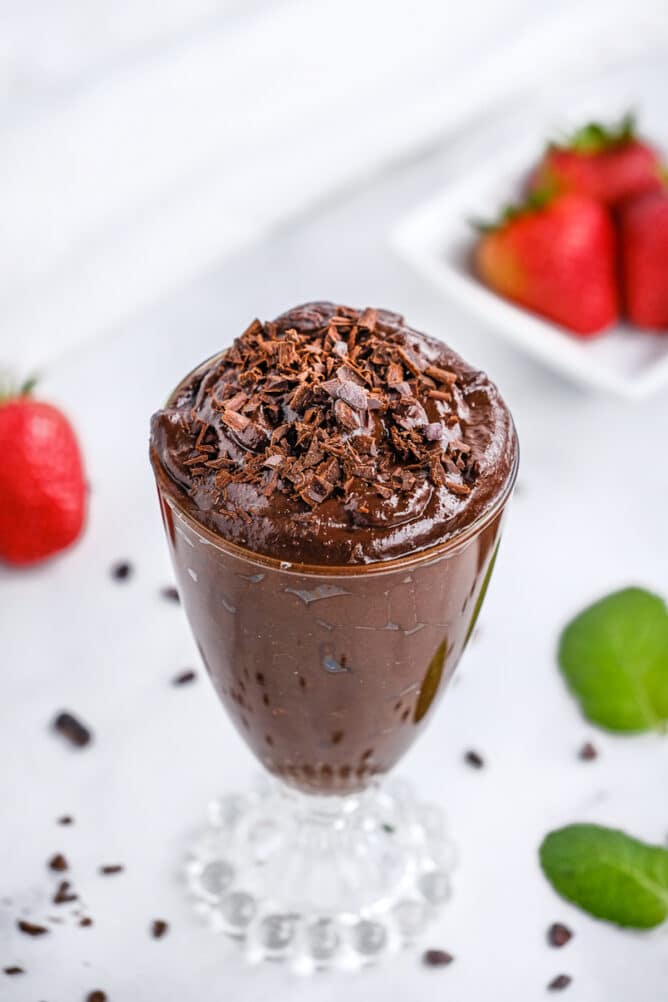 Glass pudding cup filled with avocado chocolate mousse with strawberries and mint on table