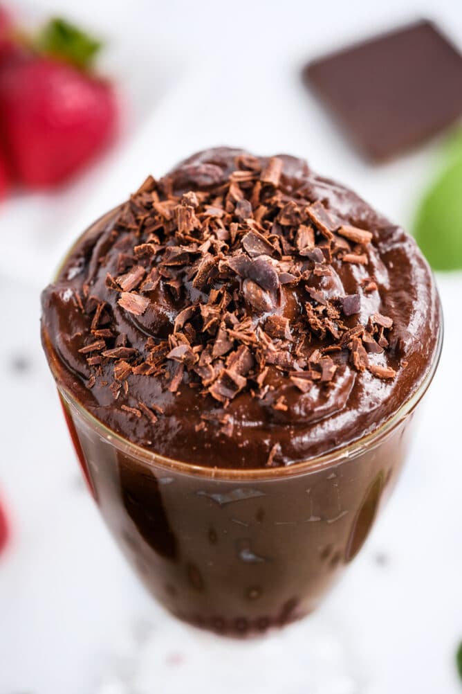 Overhead close up shot of avocado chocolate mousse in glass pudding dish with chocolate shavings on top