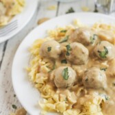 Close up photo of swedish meatballs over egg noodles on a white plate on kitchen table